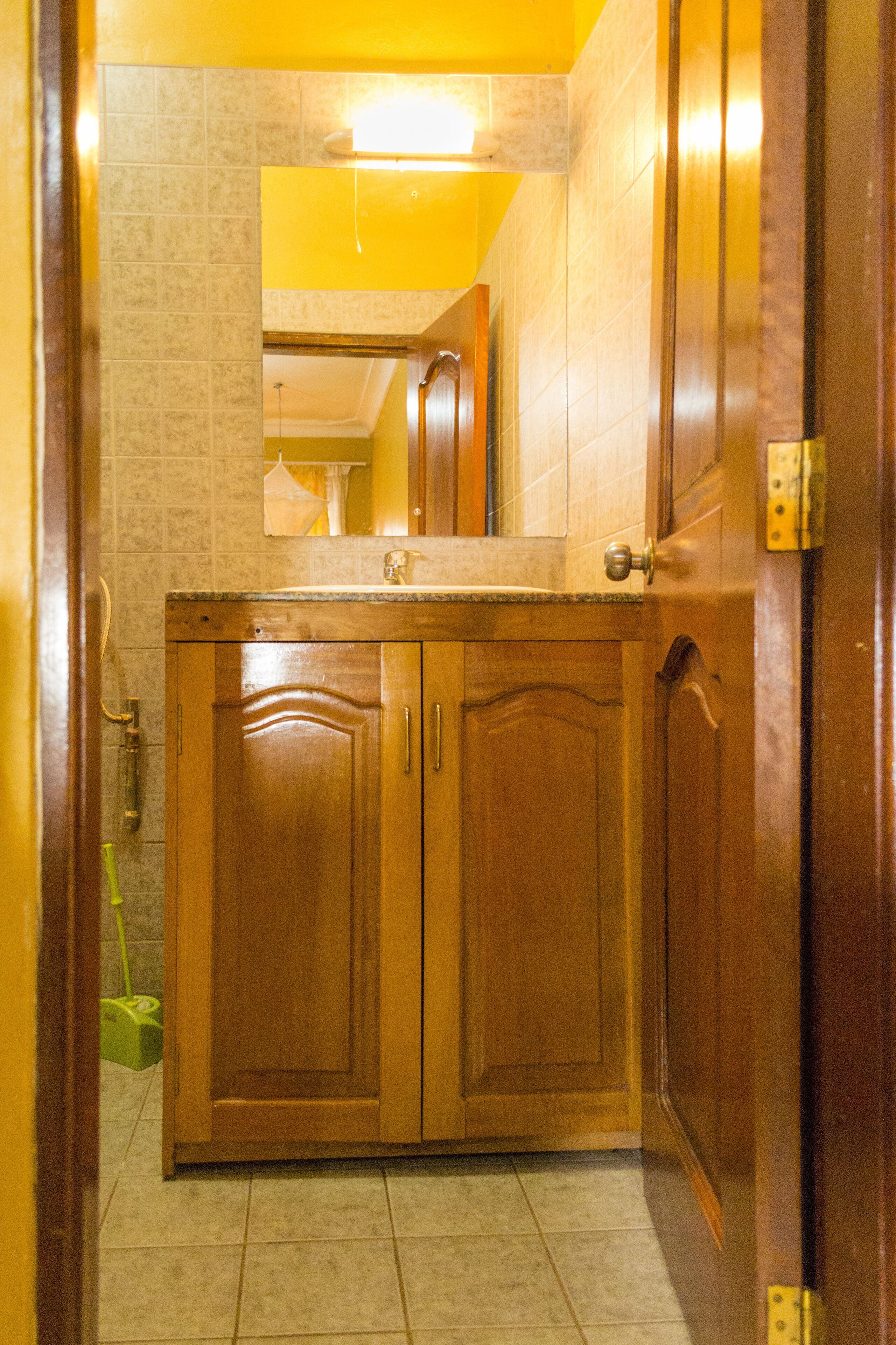 A wooden bathroom vanity with a mirror above it, a sink, and a door with a brass handle.