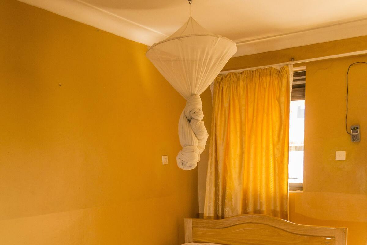 A single bed with a wooden headboard in a room with yellow walls and a tiled floor.