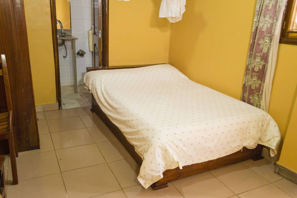 A bedroom with a bed, a wooden door, a small bathroom with a sink, and a curtain.