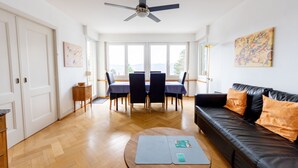 Una sala de estar amplia con comedor, un sofá de cuero negro y un ventilador de techo.