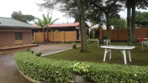 A courtyard with a brick building, a white table, and a small garden area. - Palace Motel (Fort Portal)