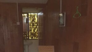 A room with a wooden floor, a table, and two wicker chairs. - Palace Motel (Fort Portal)