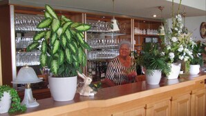 A bar area with a counter, potted plants, and shelves with glassware. - Hotel Restaurant Rheinkrone Koblenz (Koblenz)