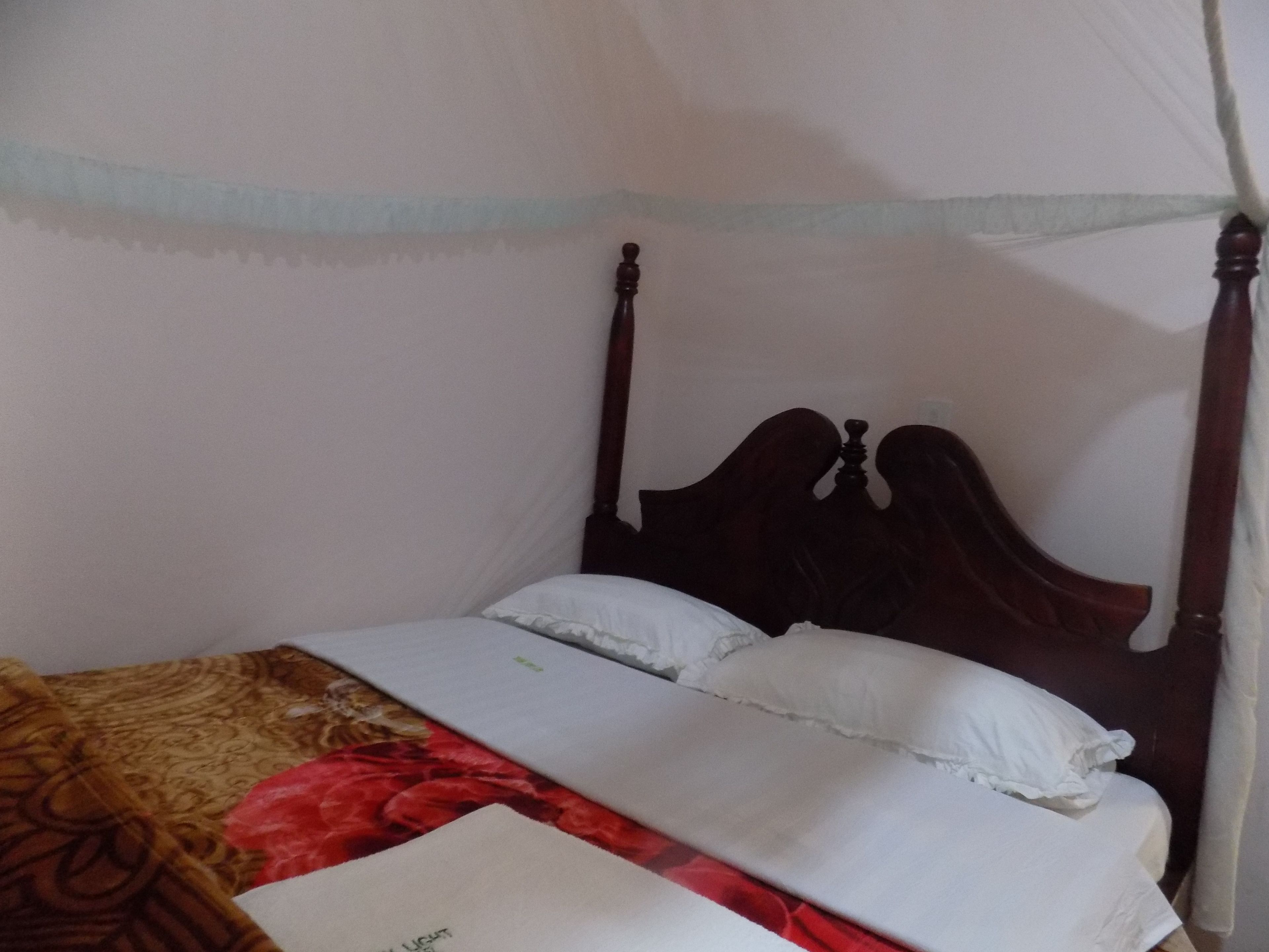 A bed with a wooden headboard, white bedding, and a red patterned blanket.