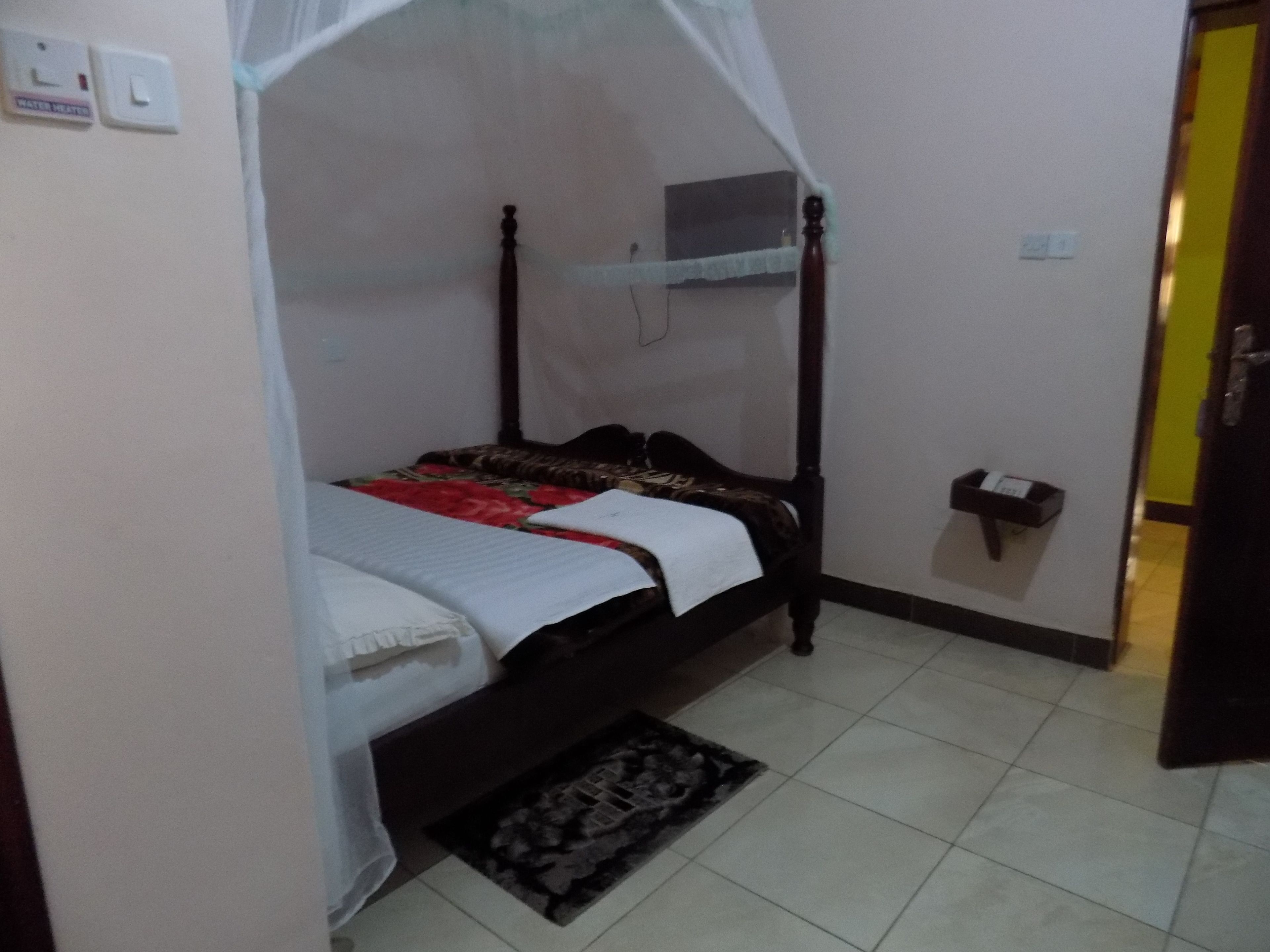 A room with a bed under a canopy, a small shelf with a telephone, and a tiled floor.