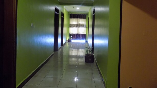 Un pasillo con paredes verdes, piso de baldosas y una ventana con cortinas.