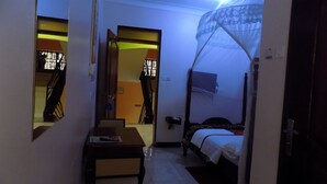 Un dormitorio con una cama bajo una mosquitera, un escritorio con una silla y una escalera que lleva a otra habitación.