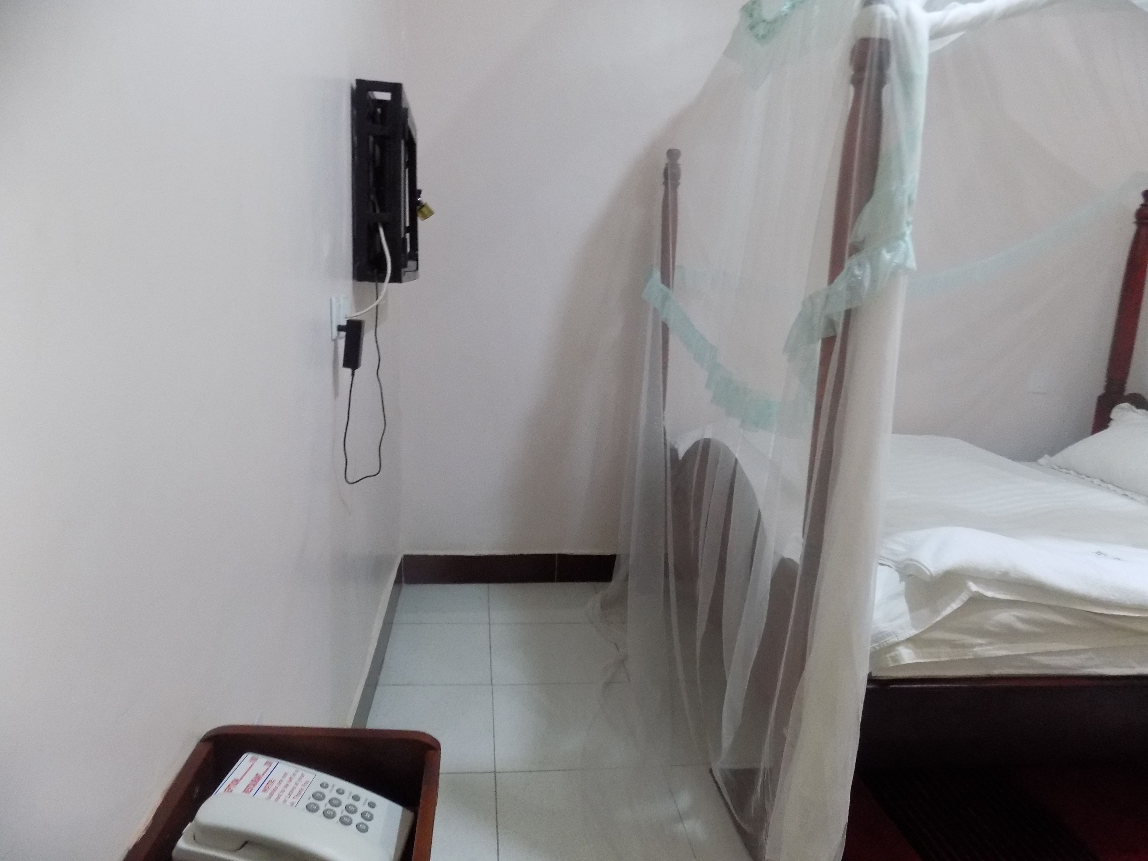 A small, simple room with a bed, a bedside table, a wall-mounted phone, and a curtain.