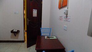 Una habitación pequeña con una mesa de madera y dos sillas azules, una puerta con un letrero, y un purificador de aire fijado a la pared.