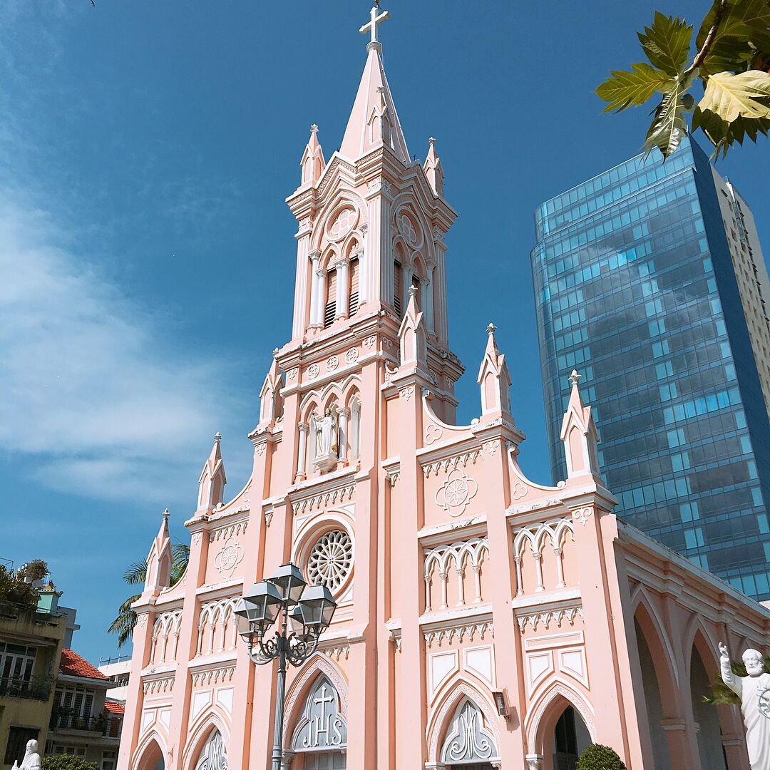 Une église rose, dotée d’un clocher imposant et d’une horloge, entourée de bâtiments modernes.