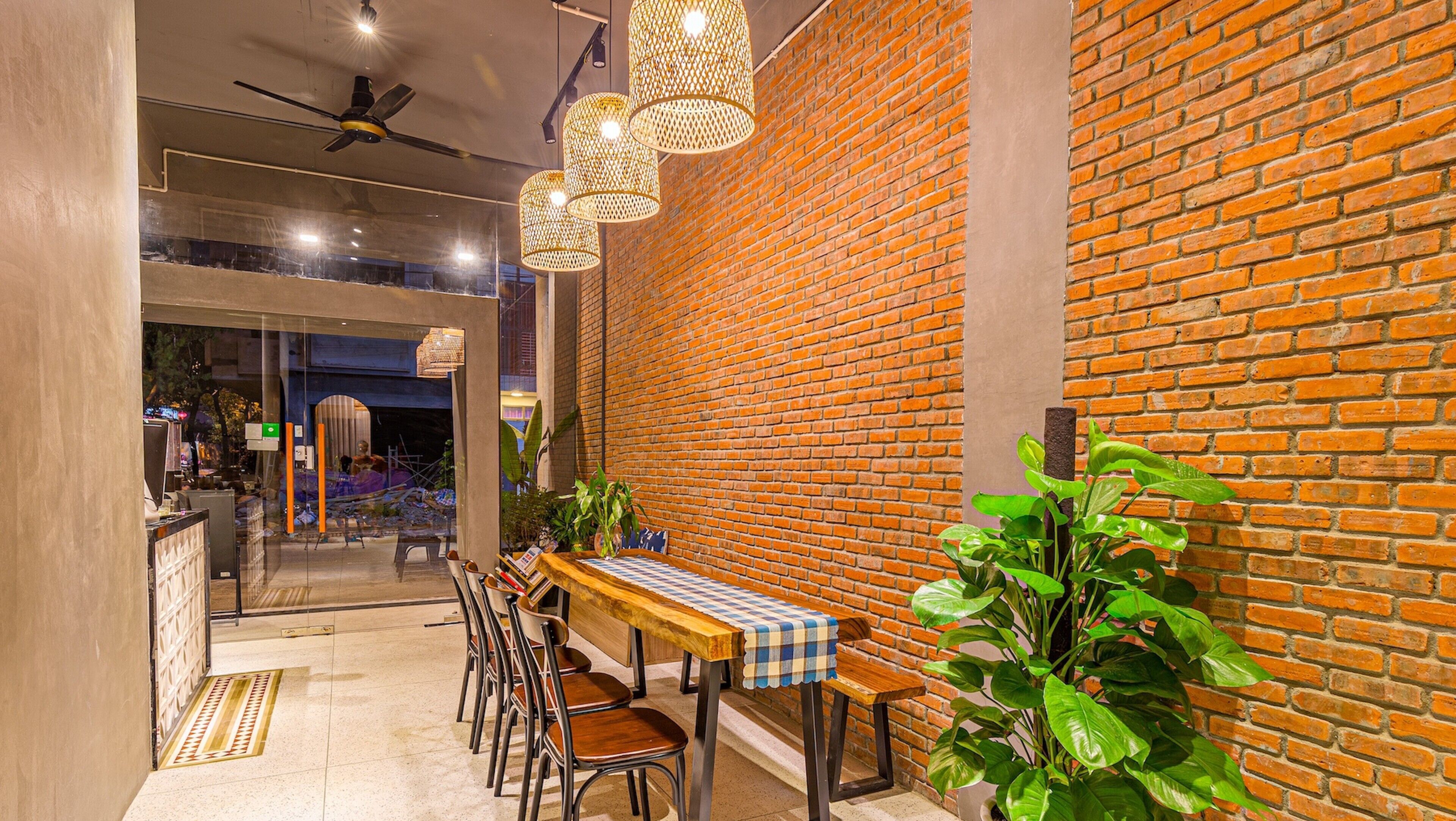 A modern interior with a brick wall, wooden tables, chairs, hanging lights, and potted plants.