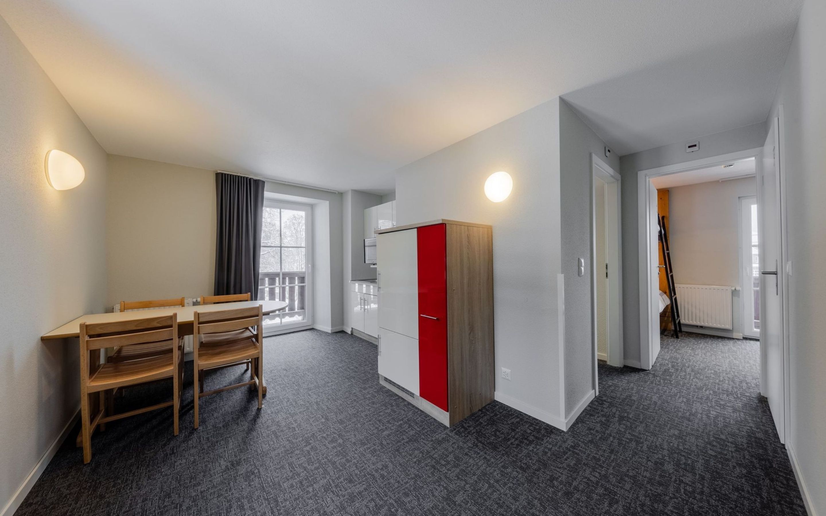 A modern hotel room with a dining area, a wardrobe, and a view of the outside.