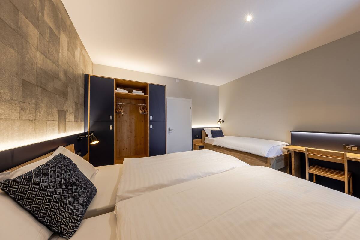 A hotel room with two beds, a wardrobe, a desk, and a bedside table.