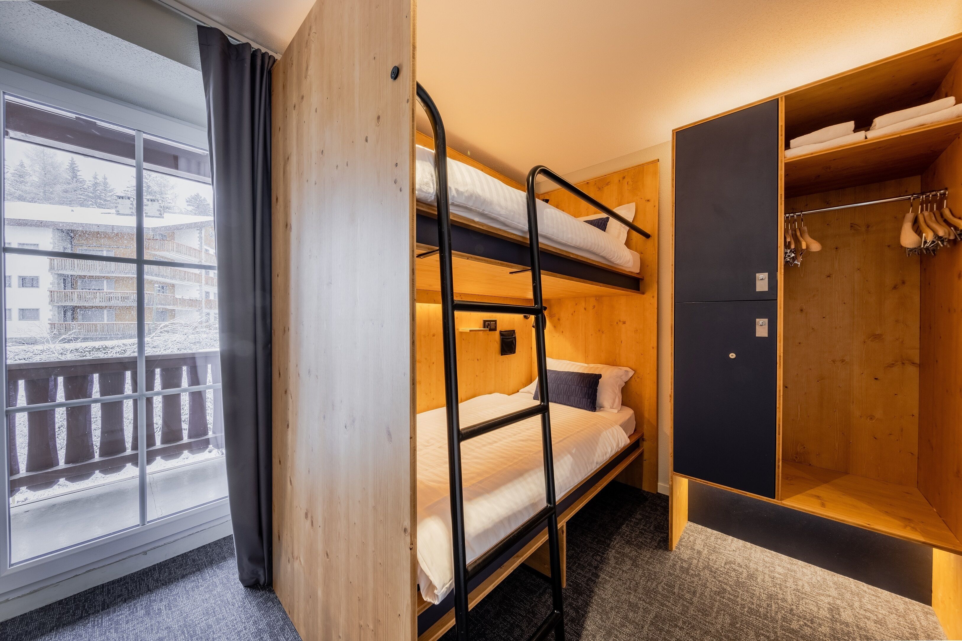 A bunk bed room with a wooden wardrobe and a window with a view of a snowy balcony.
