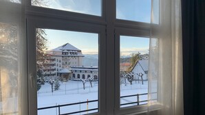 Une fenêtre donnant sur un paysage enneigé, avec des bâtiments et une chaîne de montagnes.