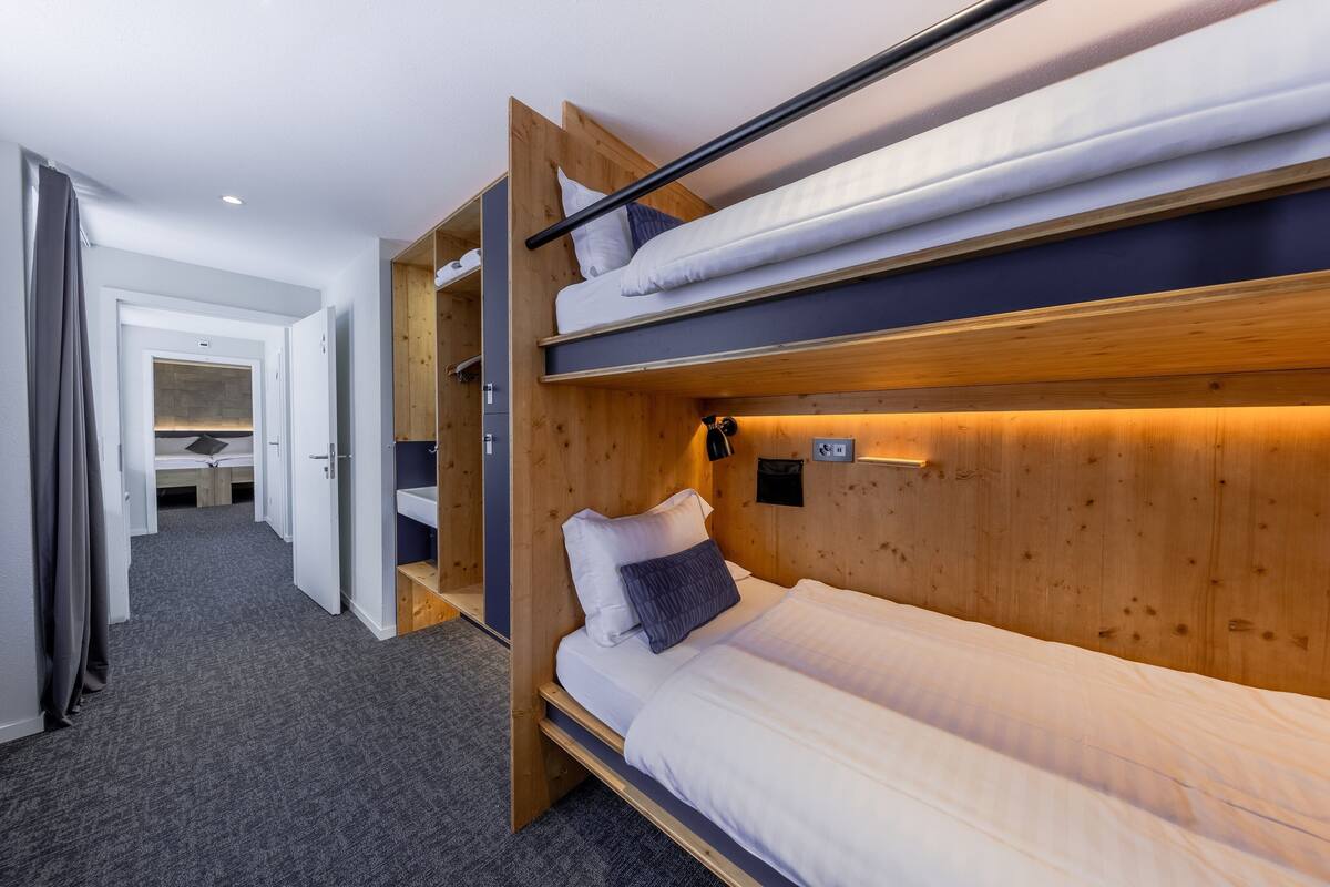 A bunk bed room with a wooden headboard, a bedside table, and a wall-mounted light.
