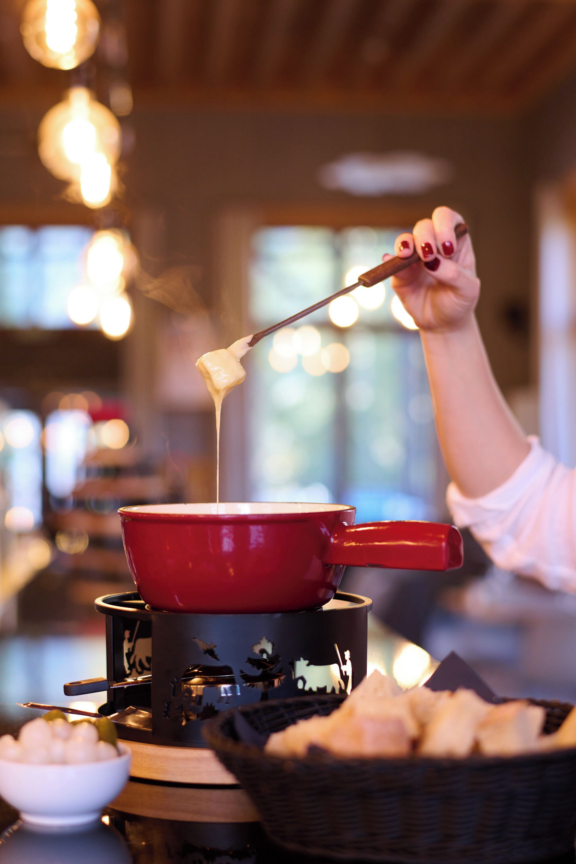 A red pot on a portable stove with a hand dipping a piece of bread into melted cheese.