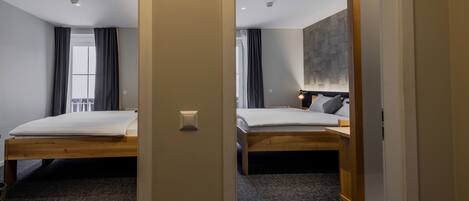 Une chambre d’hôtel avec deux lits, une grande fenêtre avec des rideaux, un lampadaire fixé au mur et un sol recouvert de moquette.