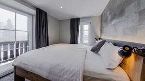 Une chambre d’hôtel moderne avec un grand lit, une tête de lit dotée d’un luminaire et une vue sur l’extérieur par une fenêtre.