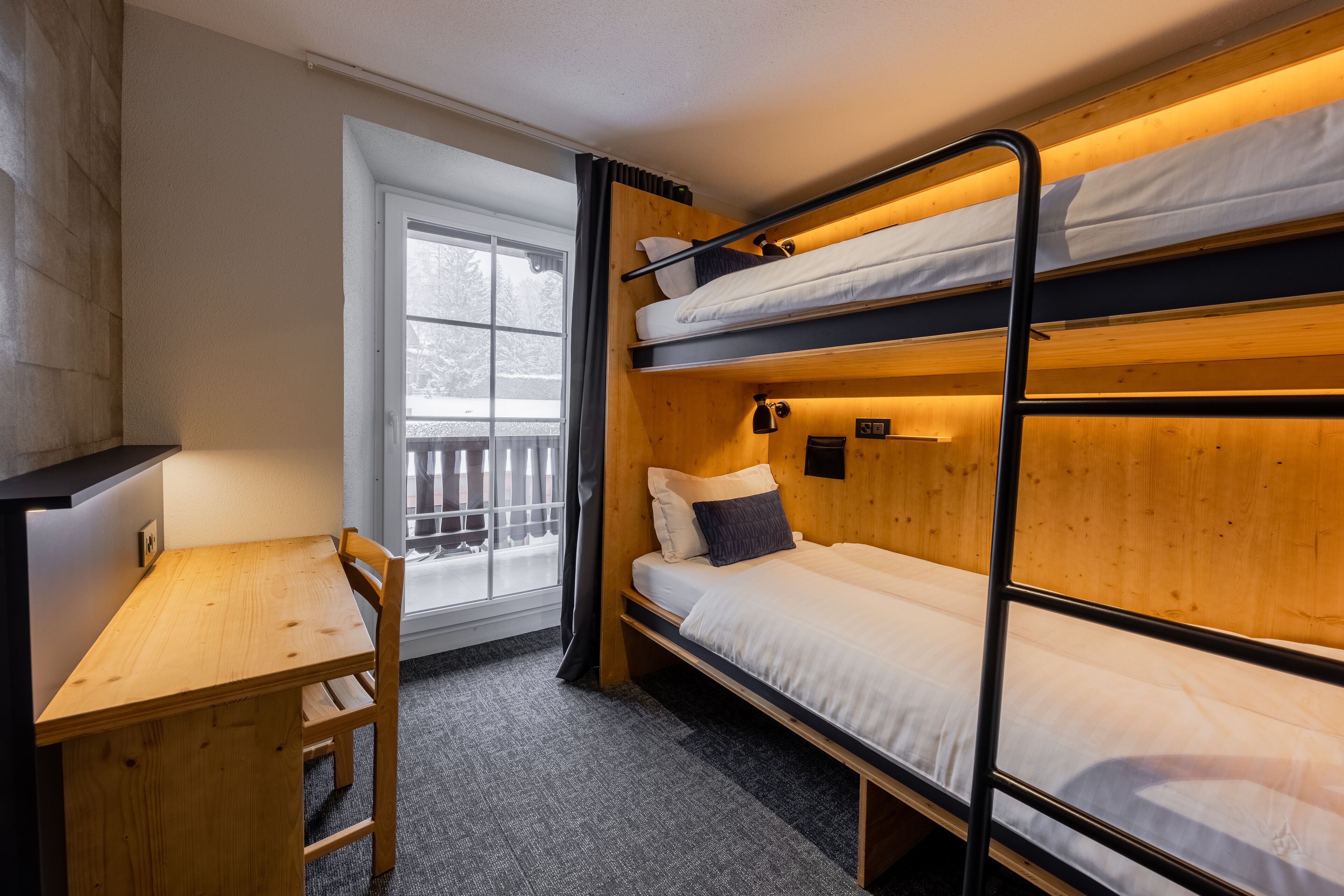 Une chambre avec un lit superposé, un bureau et une chaise, une fenêtre avec vue et une petite table.