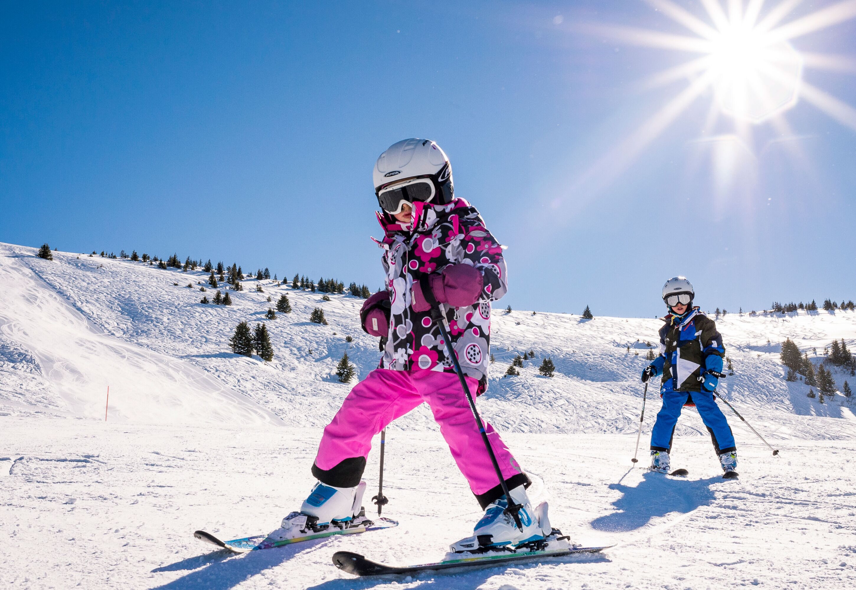 Une piste de ski enneigée avec deux skieurs portant des tenues colorées.