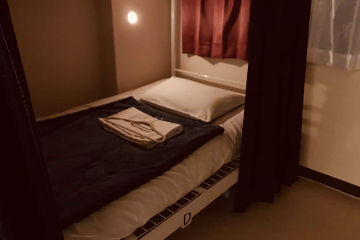 Una cama individual con un colchón blanco y una manta oscura.