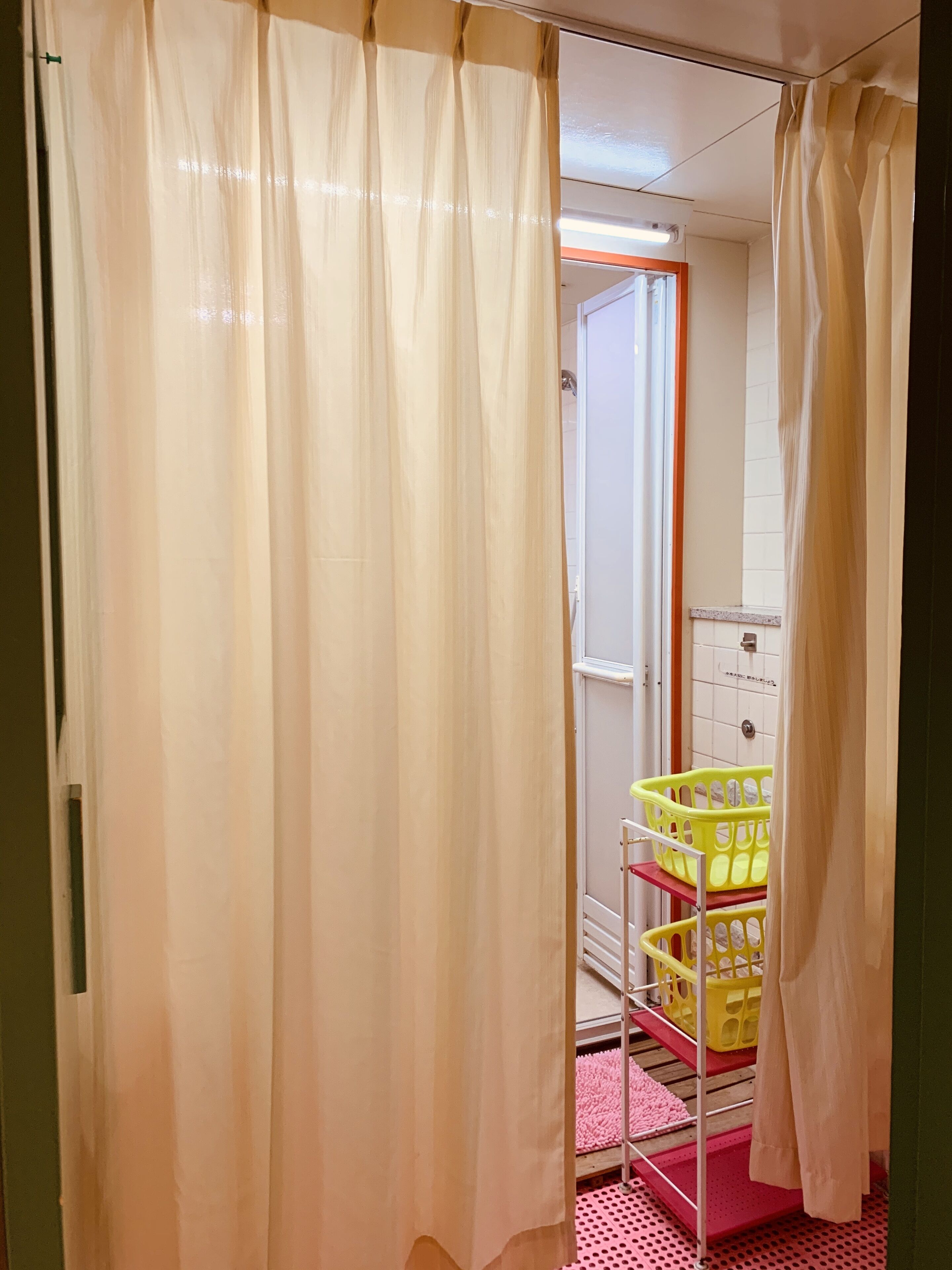 Une pièce avec un rideau, une porte donnant sur une salle de bain et un présentoir avec des paniers jaunes.