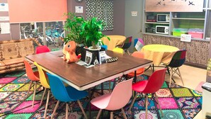 Une pièce avec une table en bois, des chaises colorées, un jouet en peluche, une plante en pot et une carte du monde accrochée au mur.