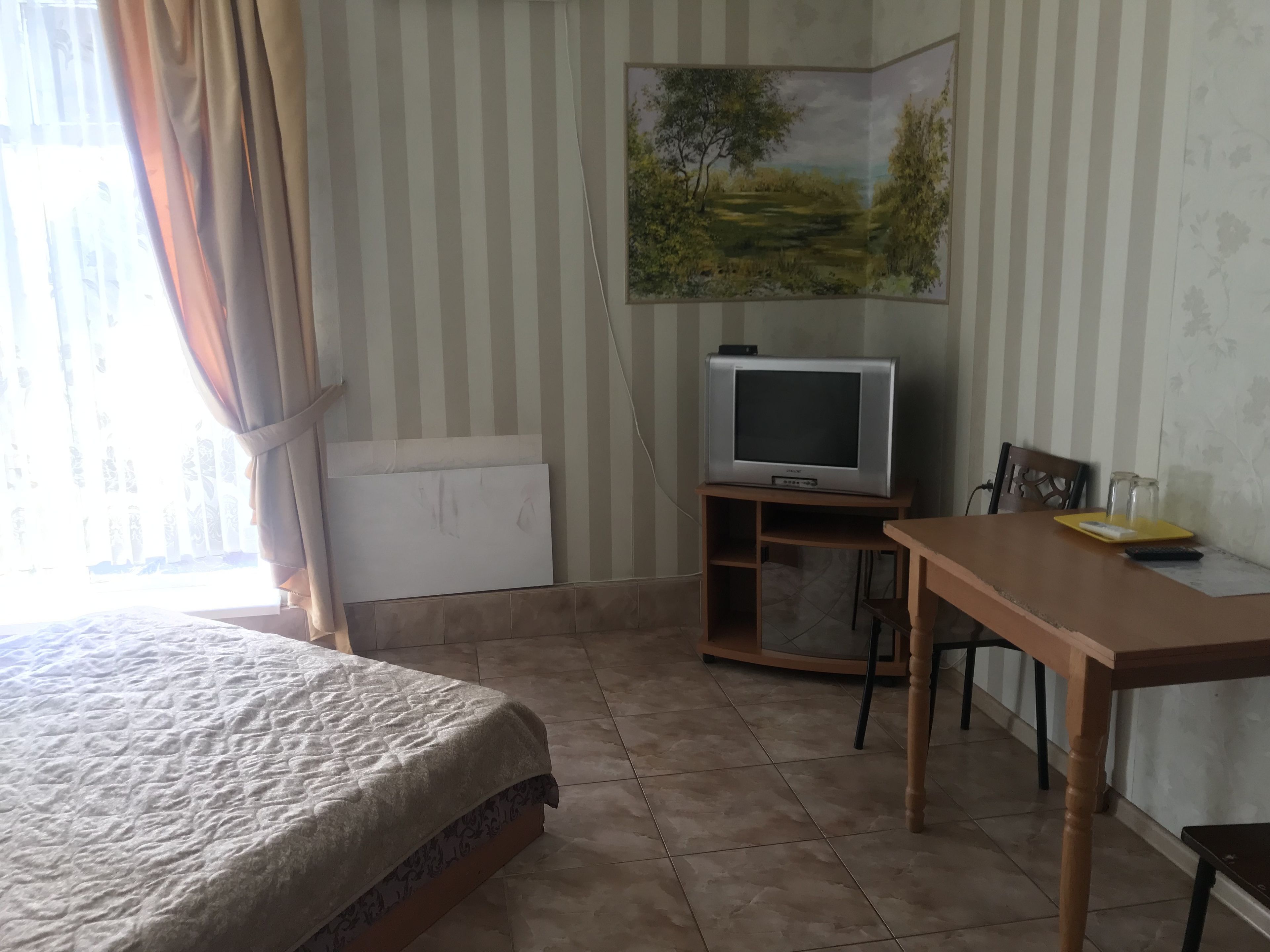 Quarto de hotel com uma cama, televisão sobre suporte de madeira, mesa e uma cadeira.