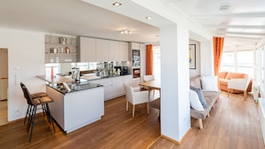 A modern kitchen with white cabinets, a central island, and a dining area with a table and chairs. - Skyflats Vienna Belle View (Vienna)