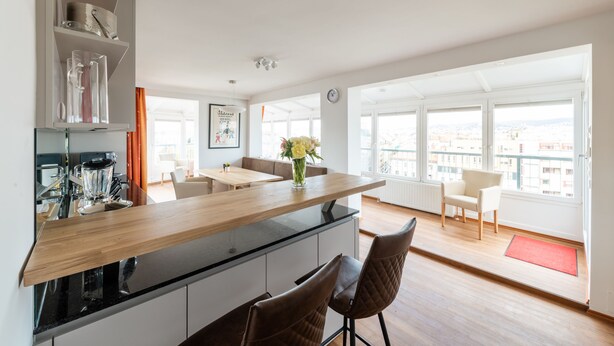 A modern kitchen with a wooden countertop, black appliances, and a dining area with a red rug. - Skyflats Vienna Belle View (Vienna)