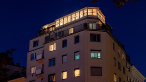 A multi-story building with illuminated windows and balconies, featuring a corner entrance and a visible ground-floor entrance. - Skyflats Vienna Belle View (Vienna)