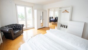 A bedroom with a bed, a black leather sofa, a wardrobe, and a dining area with a table and chairs. - Sunny & Stylish 3 Bedroom Apartment, 20 min from city centre. 1st Floor. (Kreis 7)