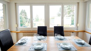 A dining area with a wooden table set for four, large windows, and black chairs. - Sunny & Stylish 3 Bedroom Apartment, 20 min from city centre. 1st Floor. (Kreis 7)