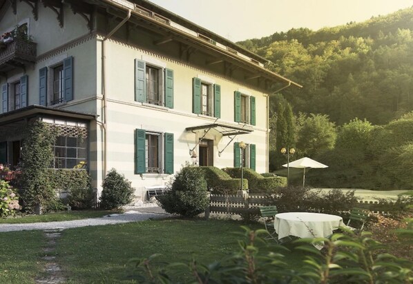 A two-story building with a balcony, a covered porch, and a table with a canopy. - Au Vieux Manoir (Monthey)