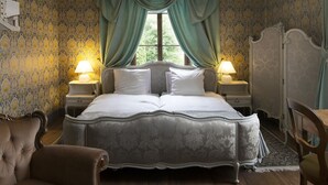 Una cama clásica con dosel y dos lámparas de noche, con una colcha de estampado floral y cortinas verdes con drapeado.