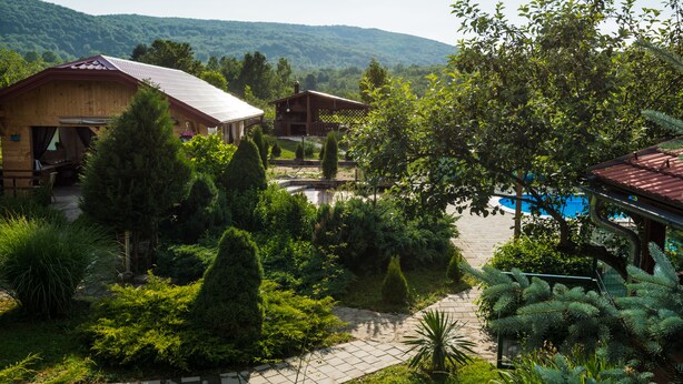 A rustic lodge with a stone pathway, surrounded by lush greenery and a mountain backdrop. - Villa Rubčić Rooms & Pansion (Rakovica)