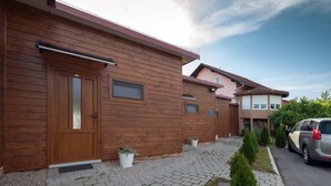A modern wooden house with a garage door, a small garden with potted plants, and a paved driveway. - Villa Rubčić Rooms & Pansion (Rakovica)