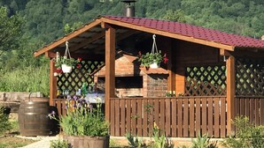 A rustic outdoor kitchen with a brick oven, wooden pergola, and hanging flower pots. - Villa Rubčić Rooms & Pansion (Rakovica)