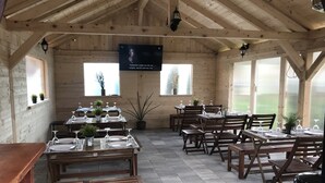 A rustic wooden dining area with tables set for dining, potted plants, and a mounted television. - Villa Rubčić Rooms & Pansion (Rakovica)