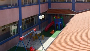 Ein mehrstöckiges Gebäude mit Spielplatz, der Schaukeln, eine Rutsche und eine Kletterkonstruktion bietet.