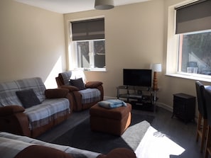 A living room with a sofa, armchair, ottoman, TV, and a lamp.