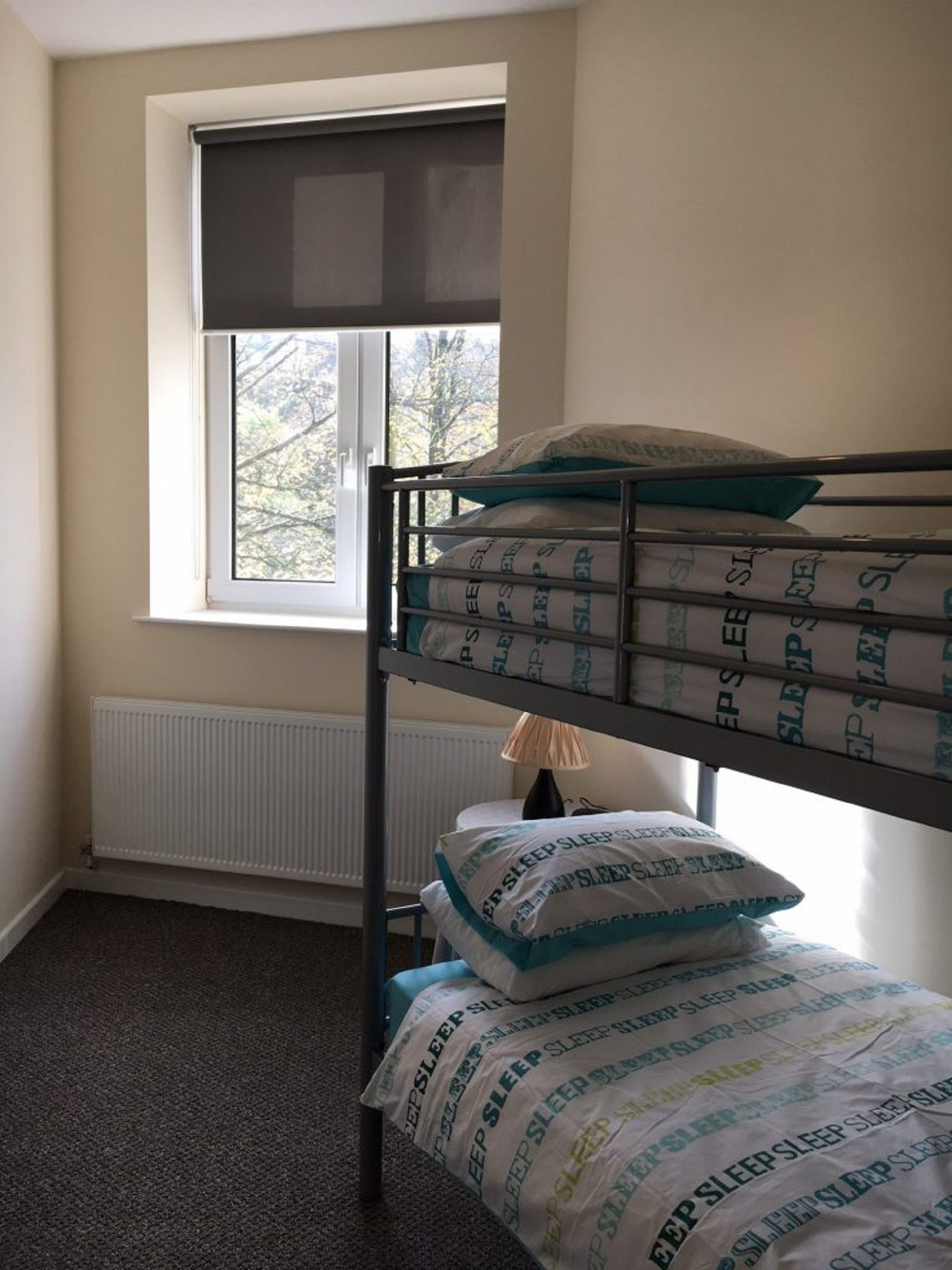 A bunk bed with pillows labeled "SLEEP SLEEP SLEEP" in a room with a window and radiator.