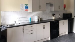 Une cuisine moderne avec des meubles gris, un plan de travail noir et un luminaire suspendu blanc.