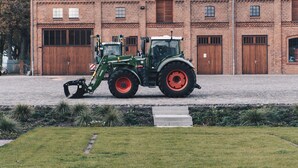 Un trattore verde parcheggiato di fronte a un edificio in mattoni con grandi porte di legno.
