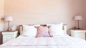 Un letto rifatto con cura, con lenzuola bianche e rosa, due comodini con lampade e un quadro incorniciato su uno dei comodini.