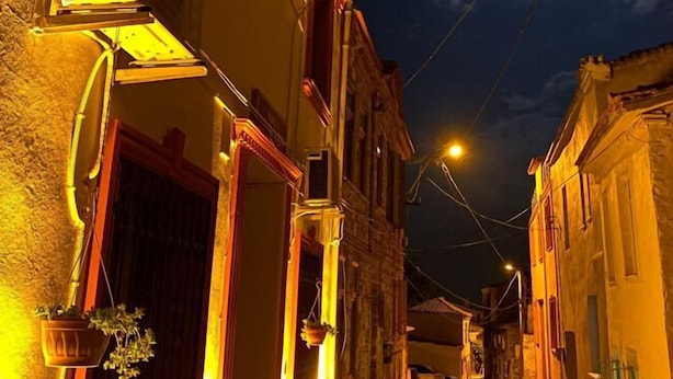 A narrow street with buildings on either side, a sign for 'SUALTI HOTEL' hanging above, and a visible moon in the sky. - Sualti Otel (Ayvalik)