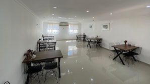A spacious dining area with multiple tables and chairs, large windows with curtains, and ceiling lights. - Sualti Otel (Ayvalik)