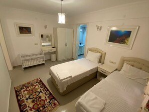 A bedroom with two beds, a crib, a wardrobe, a mirror, and a rug.