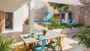 Un patio con una mesa lista para el desayuno, rodeado de sillas, un toldo blanco y un muro de piedra.